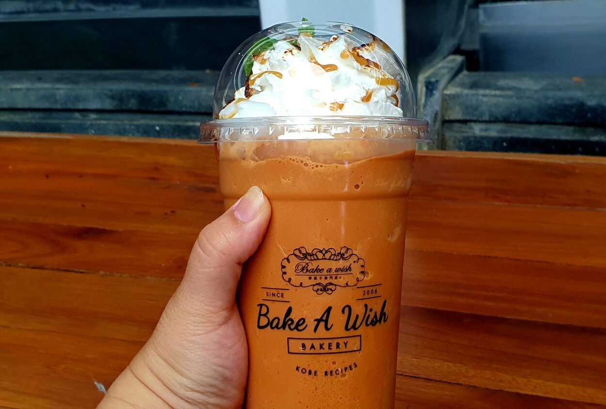 A Person Holding Thai Iced Tea With Cream Topping On It